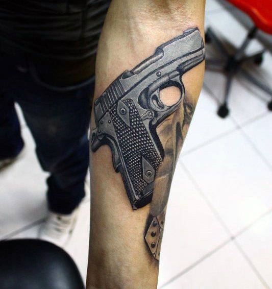 Realistic black and gray tattoo of a 1911 pistol on the forearm, featuring detailed grip texture and shading for a bold three-dimensional effect.