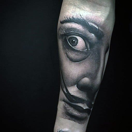 Hyper-realistic Salvador Dali portrait tattoo in black and grey, focusing on his intense eye and iconic mustache with dramatic shading.