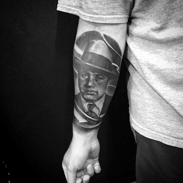 Al Capone tattoo on the forearm featuring a black-and-white portrait of the gangster with his signature fedora, surrounded by a circular design.