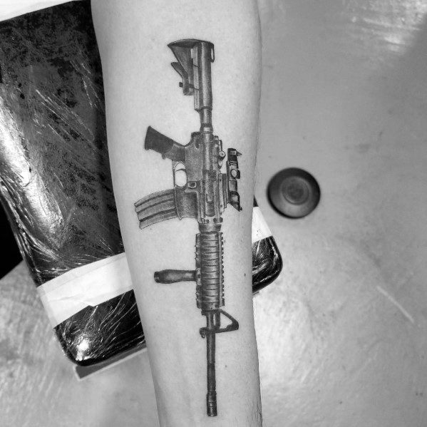 Realistic black and grey AR-15 tattoo on the forearm, featuring detailed shading, a tactical grip, and a scope, symbolizing strength and precision.