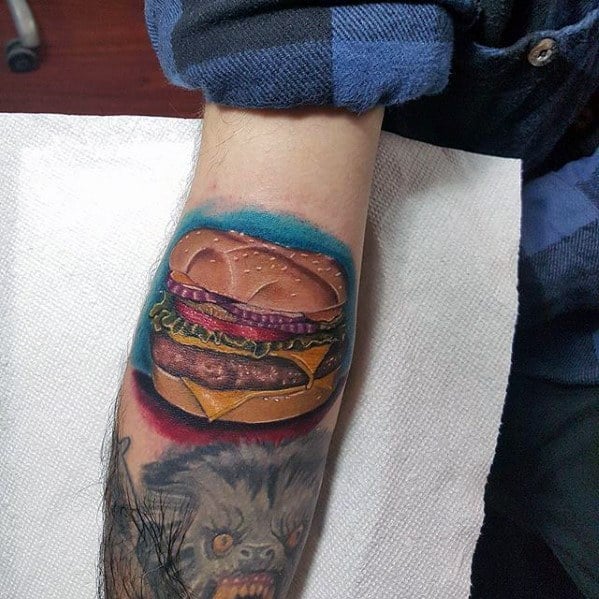A colorful tattoo of a juicy cheeseburger adorns the person's arm