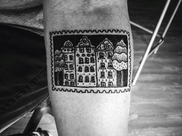 Blackwork tattoo of a postage stamp featuring a scenic row of buildings and trees.