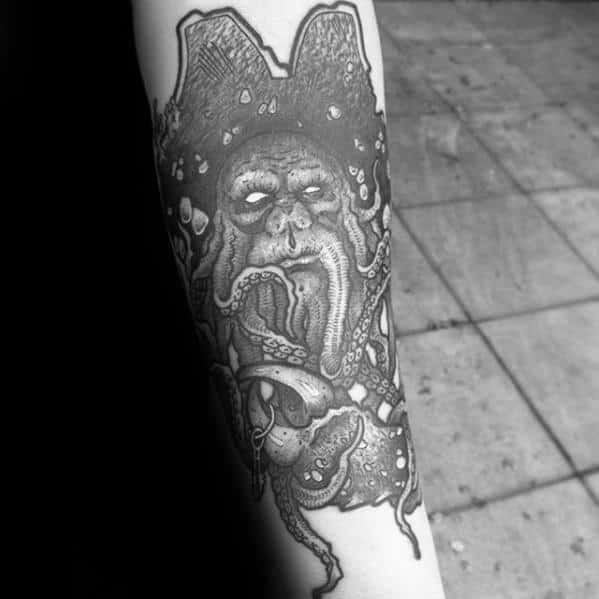 Black and white tattoo of a Davy Jones-like face with tentacles on an arm