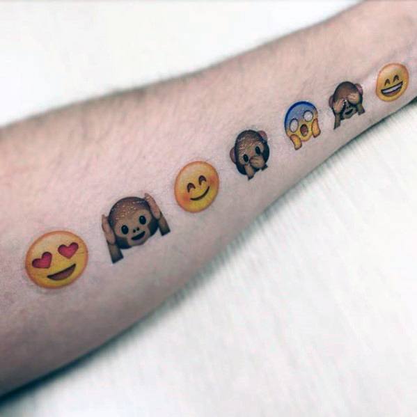 Tattoo of colorful emojis on a forearm, including heart eyes, smiling face, monkey covering eyes, shocked face, and grinning face