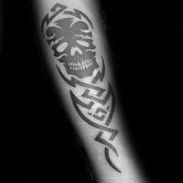 Tribal skull tattoo on forearm with sharp geometric lines and bold black shading, merging skull details with angular tribal art.