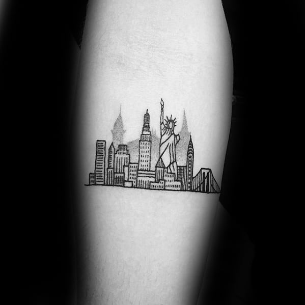 Simple black line tattoo of the New York City skyline on the upper arm, featuring the Statue of Liberty and iconic buildings.