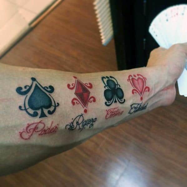 Tattoo of playing card suits on forearm with words "Poder," "Riqueza," "Felicidad," and "Euforia"