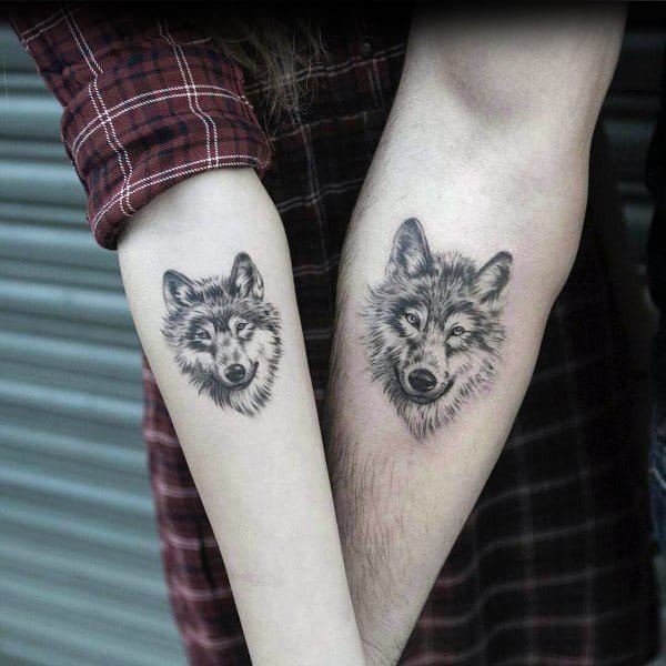 Matching forearm tattoos of realistic wolf faces, symbolizing loyalty, strength, and a deep, instinctive connection between partners.