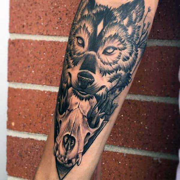 Forearm tattoo of a wolf's head above a skull and antlers