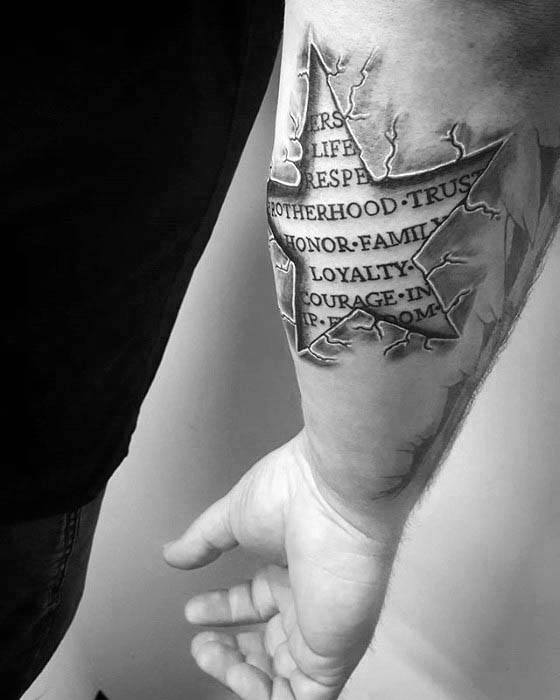 3D star tattoo on forearm with torn skin illusion, exposing bold words like brotherhood, family, and courage in a carved stone style.