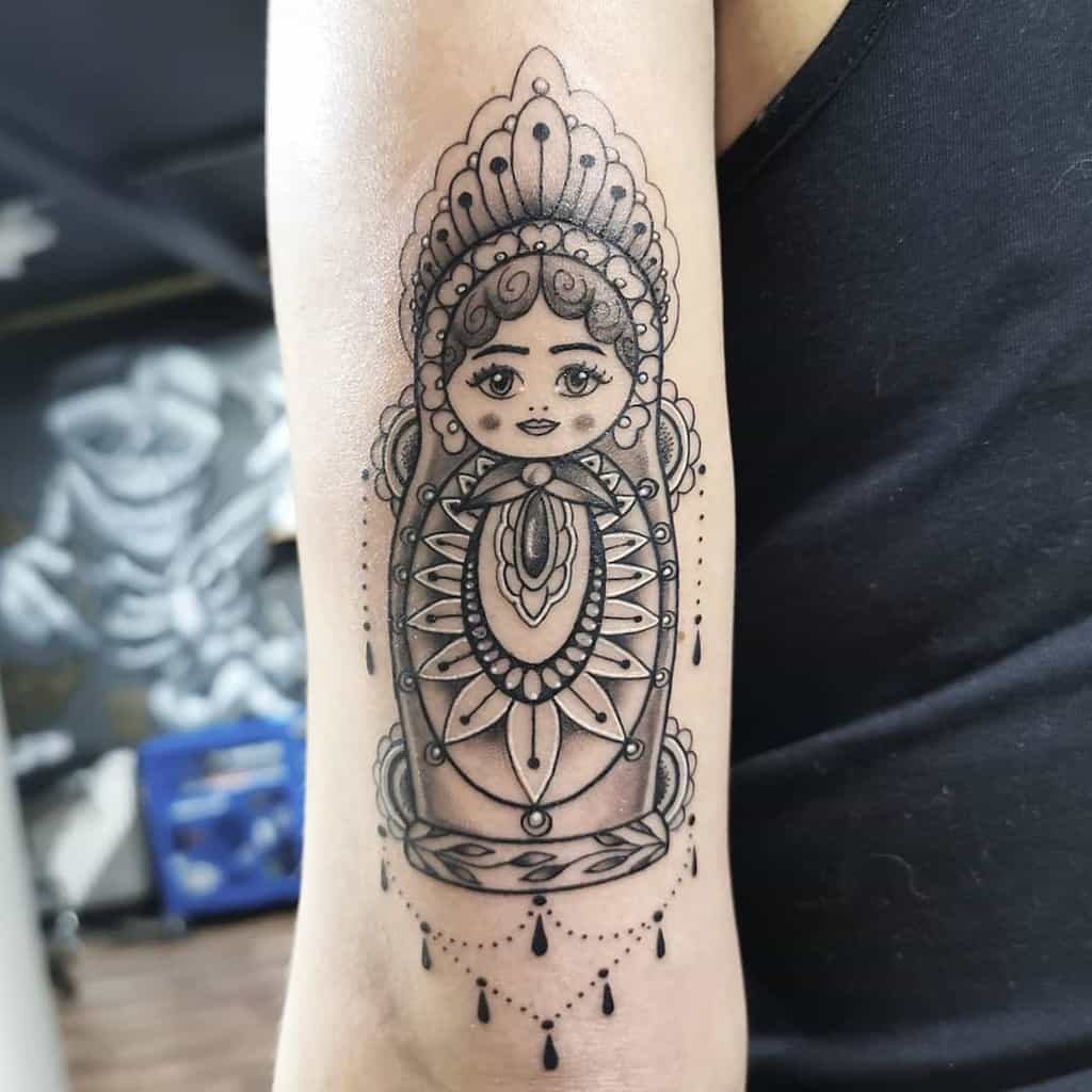 Intricate black ink tattoo of a Russian Matryoshka doll with ornate patterns, delicate shading, and decorative beaded elements
