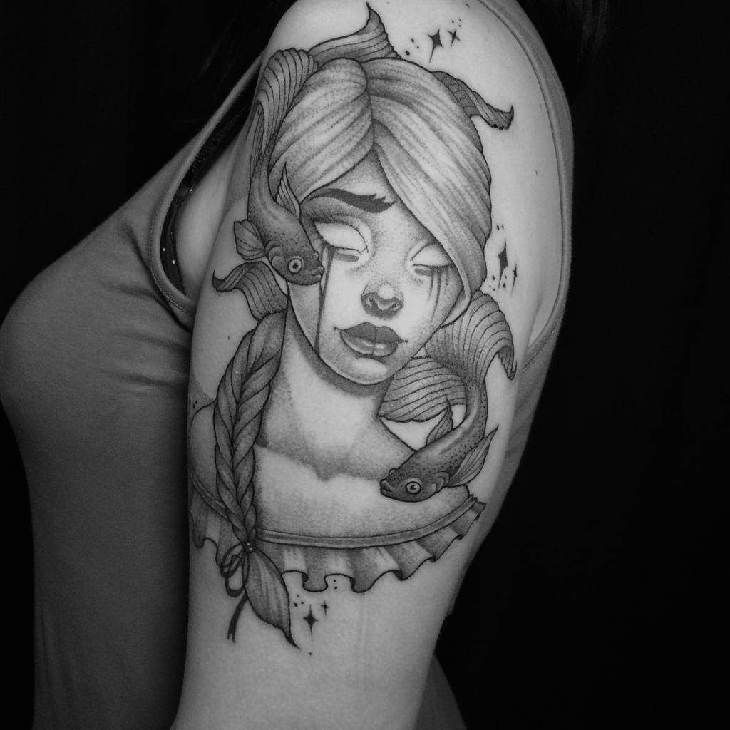 A tattoo of a woman with closed eyes, braided hair, sparkles and fish swimming around her