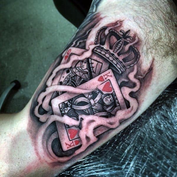 Realistic tattoo of a King of Hearts playing card with a crown, surrounded by smoke-like shading for a bold design on the inner bicep