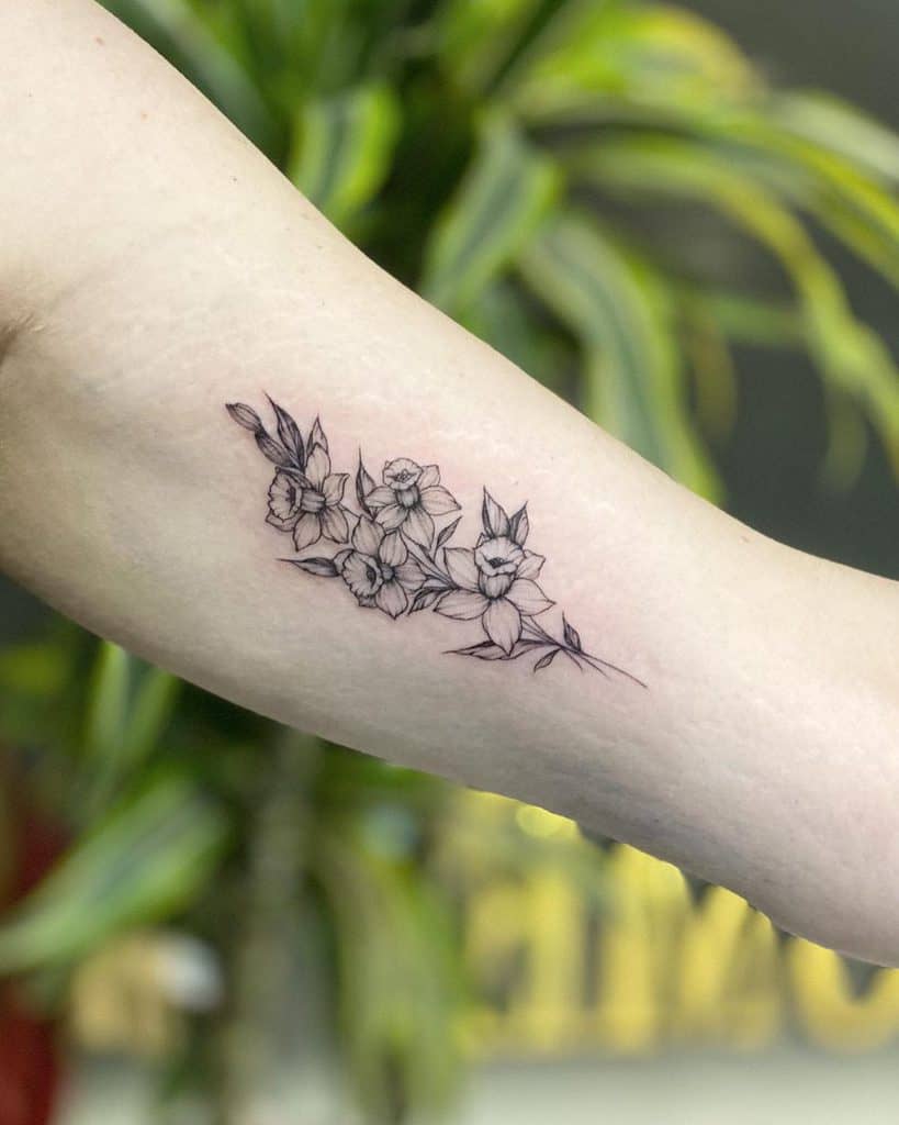 A graceful black-and-white tattoo of a cluster of daffodils, delicately arranged with fine lines and soft shading.