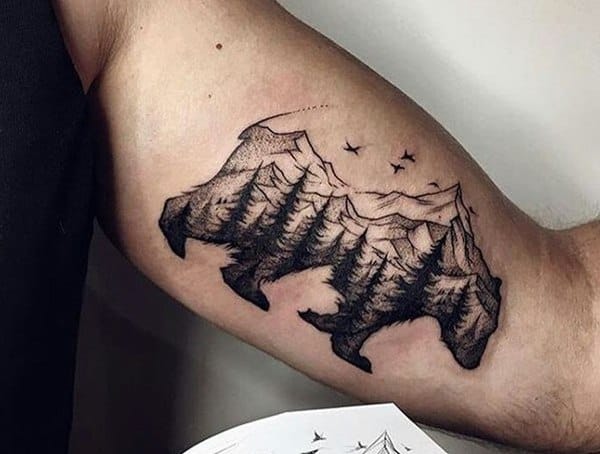 A mountain landscape tattoo shaped like a bear, with trees and birds, creating a nature-inspired design