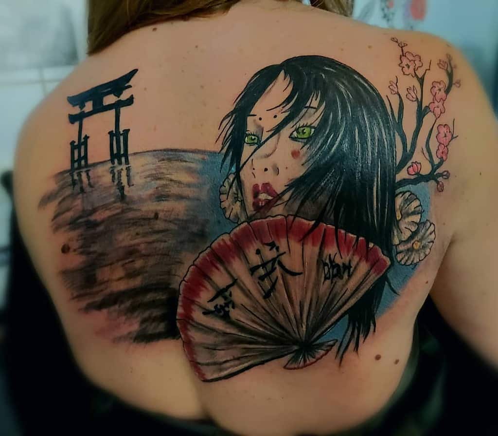 Back tattoo of a mysterious woman with green eyes holding a fan, with a torii gate over water, cherry blossoms, and Japanese calligraphy.