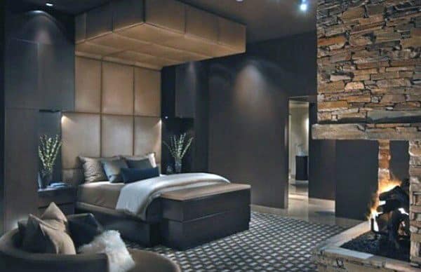 Cozy bedroom with a stone fireplace, warm lighting, and sophisticated dark-toned decor.