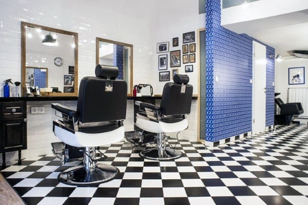 Barbershop with checkered flooring, blue patterned walls, and modern black chairs.