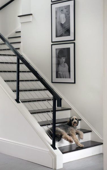 White staircase with black cable railing and framed photos on the wall in a modern interior.