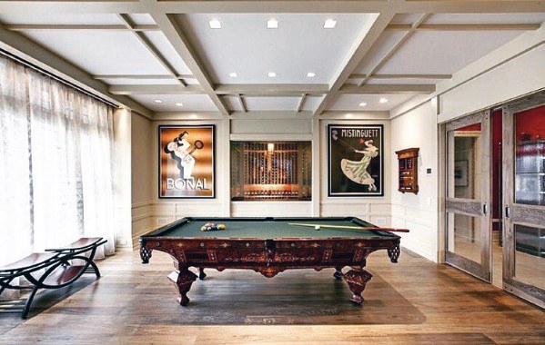 Sophisticated billiard room with vintage posters, green felt table, and coffered ceiling.