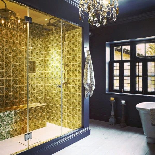 Luxurious blue bathroom with gold-tiled shower, chandelier, and freestanding bathtub.