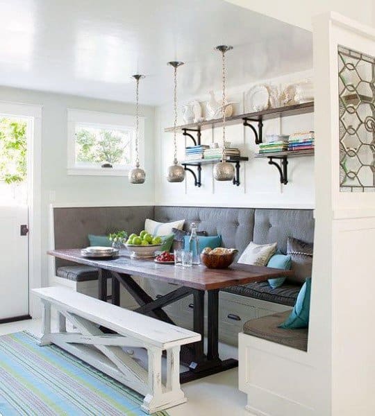 Cozy breakfast nook featuring a wooden table, bench seating, cushions, hanging lights, and decorative shelves