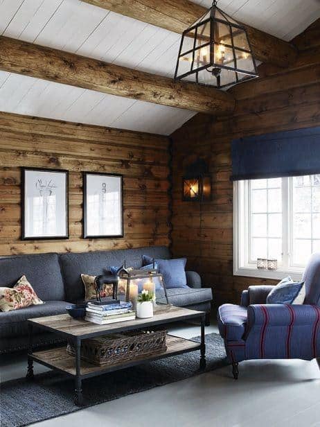 Rustic log cabin living room with wood walls, cozy seating, and natural light from large windows.