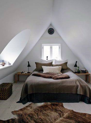 Cozy attic bedroom with a sloped ceiling, warm brown and beige bedding, two side tables, and a small window