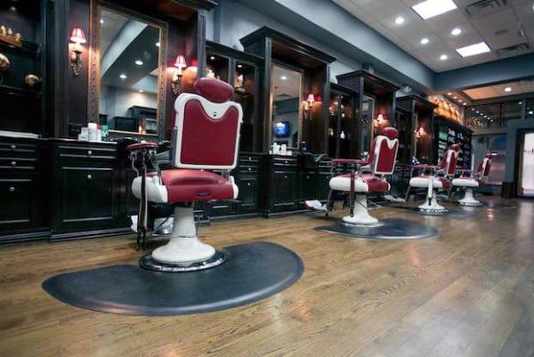 Barber shop with red vintage chairs, dark wood stations, and warm lighting on wooden flooring.