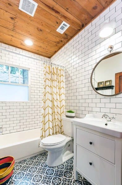 Small bathroom with wood ceiling, subway tile walls, patterned tile floor, and round mirror.