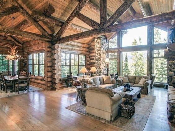 Spacious log cabin living area with vaulted ceiling, large windows, and rustic wooden accents.
