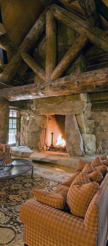 Log cabin living room with a large stone fireplace, exposed beams, and cozy patterned furniture.