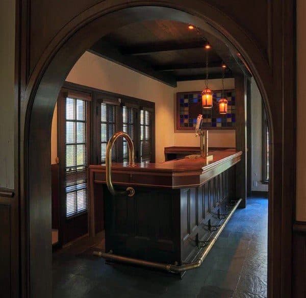 Rustic basement bar with dark wood ceiling, arched entryway, and warm pendant lighting.