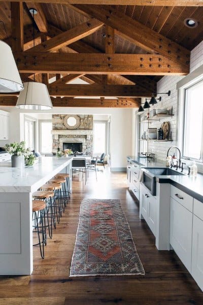 exposed ceiling beams in rustic white kitchen with fireplace and floor rug 