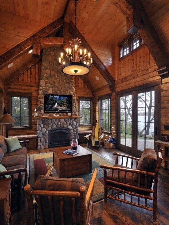 Cozy log cabin living room with stone fireplace, vaulted ceiling, and rustic wooden furniture.