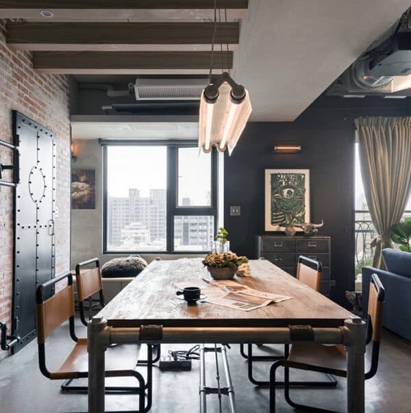 Industrial dining room with a wooden table, metal pipe frame, and exposed brick wall.
