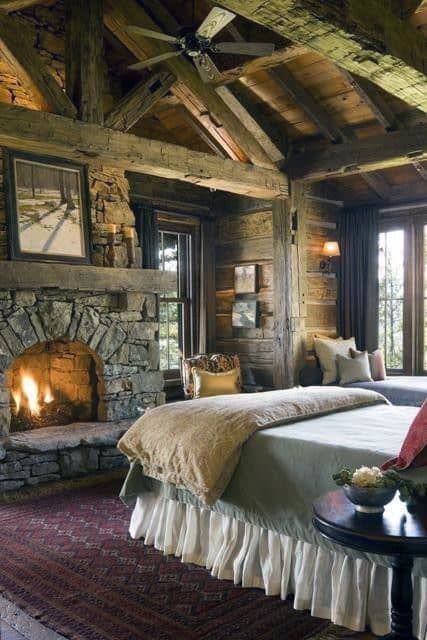 Rustic log cabin bedroom with stone fireplace, wooden beams, and cozy bedding.