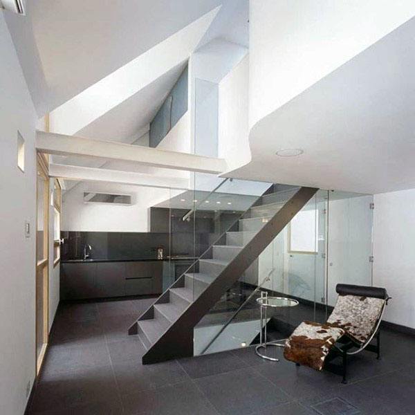 Modern interior with a sleek black kitchen, glass staircase, and lounge chair next to a small glass table