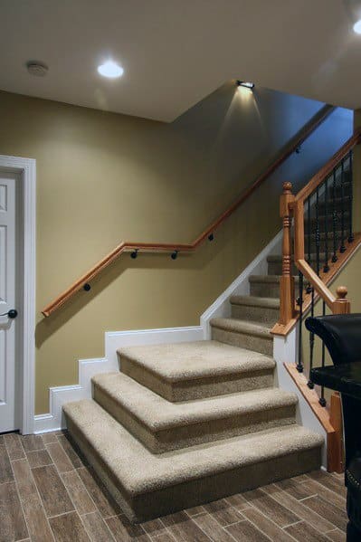 Carpeted staircase with wide descent and wooden handrail in a cozy basement space with tiled flooring.