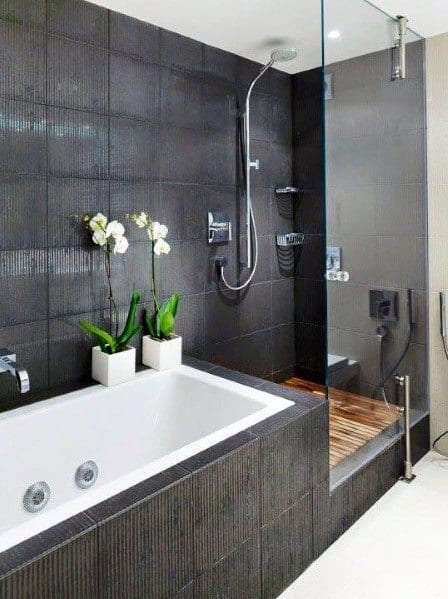 Modern bathroom with dark textured tiles, built-in tub, and glass shower with wood floor.