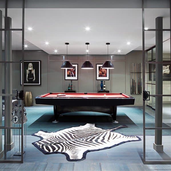 Eclectic billiard room with red felt pool table, zebra rug, and modern artwork on gray walls.