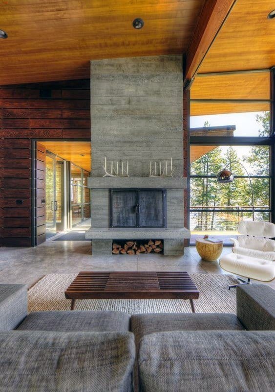 Rustic concrete fireplace with firewood storage and large windows.