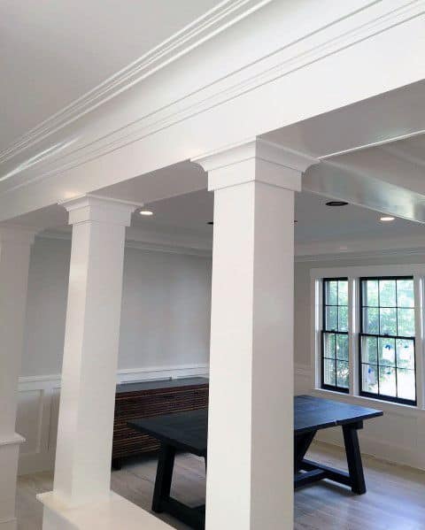 A bright interior with white crown molding, supporting columns, and large windows, creating an open and airy space