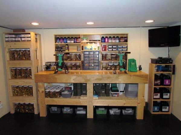 Large reloading bench with dual presses, organized shelves, labeled storage bins, and overhead lighting for efficiency