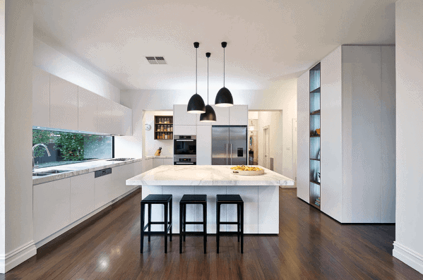 Modern white kitchen with marble island, black pendant lights, and sleek cabinetry.