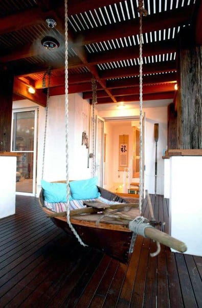 Boat-shaped hanging bed with colorful cushions, rope supports, and a wooden patio setting.