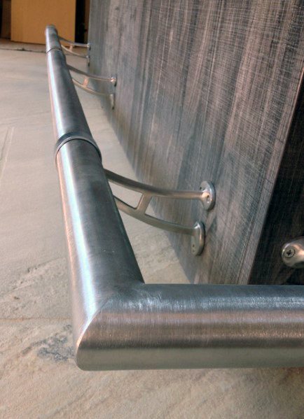 Satin stainless steel foot rail mounted to a wooden bar with curved brackets on a smooth concrete floor.