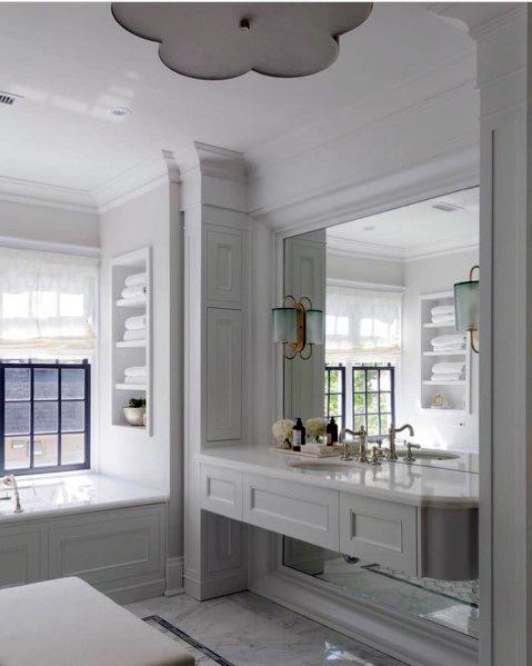 Modern white vanity with large mirror, built-in shelving, and elegant wall sconces.
