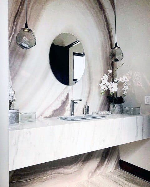 Modern bathroom with marble wall, floating vanity, round mirror, and pendant lights.