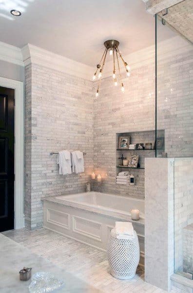 Elegant bathroom with white marble tile walls, built-in tub, and modern chandelier.
